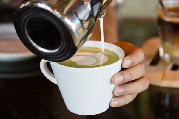 Barista hands pouring milk making hot green tea