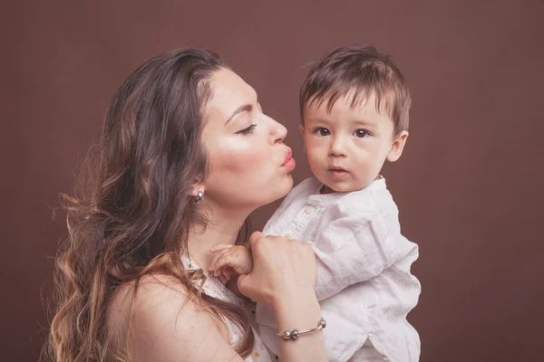 Mother kissing her baby child son on brown background
