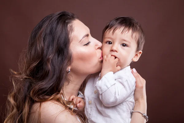 Mother kissing her baby child son on brown background