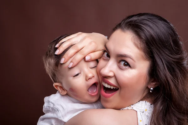 Laughing mother with her baby son in hands on brown background i