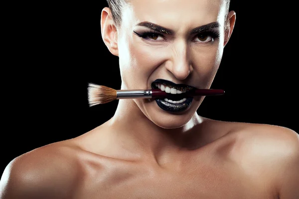 Woman with make up brush in mouth on black background