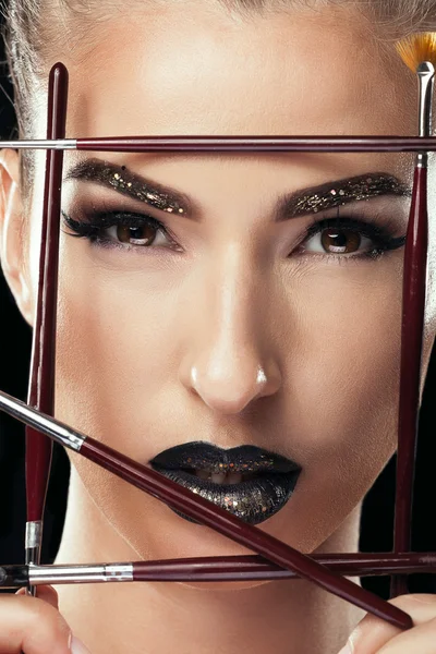 Woman with make up brushes and black lips