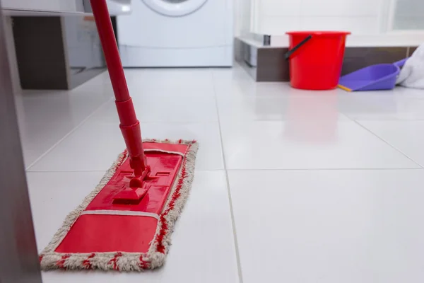 Colorful red mop on a clean white tiled floor