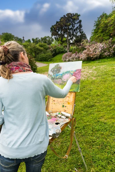 Back view of female painter finishing her picture in a garden