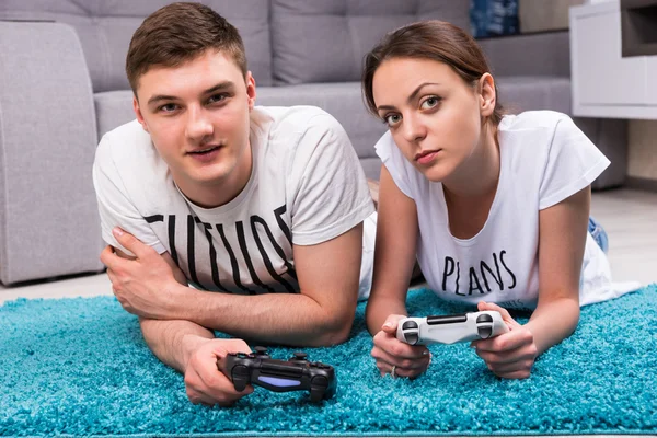 Fasionable pair lying on a rug playing video games