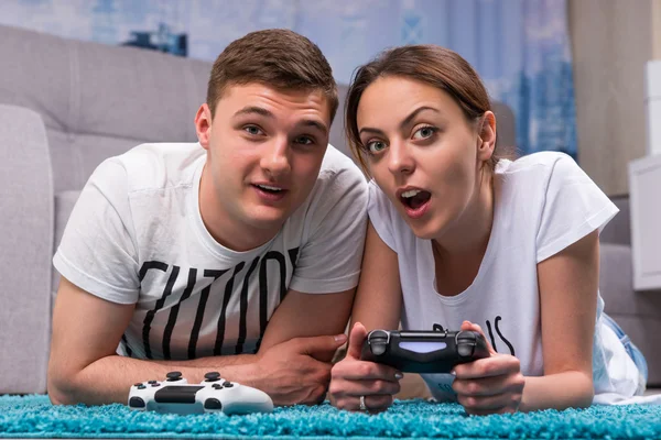 Emotional young couple lying on a rug and playing video games