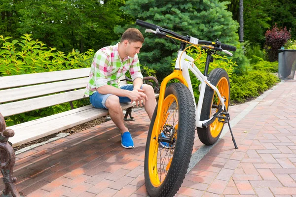 Lonely man in shorts sitting on bench near bike
