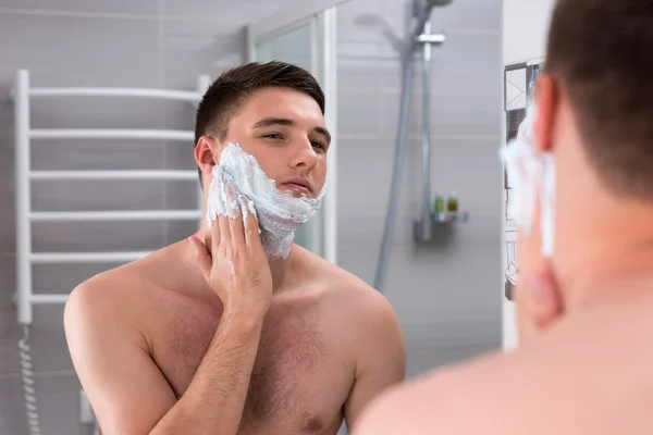Young male smearing foam for shave on his face