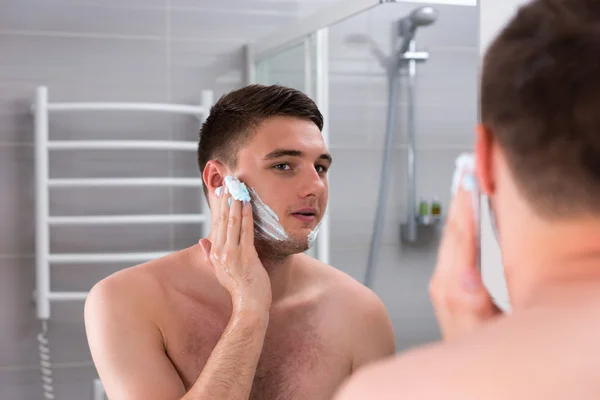 Guy smearing shaving gel on his face in the bathroom