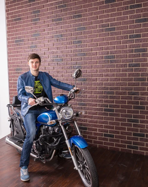 Young Man on Blue Motorcycle by Brick Wall