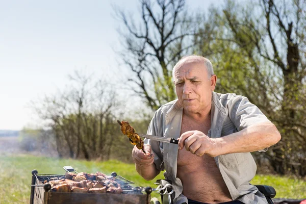 Happy Old Man Checking Grilled Meat with Knife