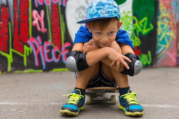 Smiling Boy Sitting on Skateboard Hugging Knees