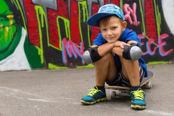 Smiling Boy Sitting on Skateboard Hugging Knees