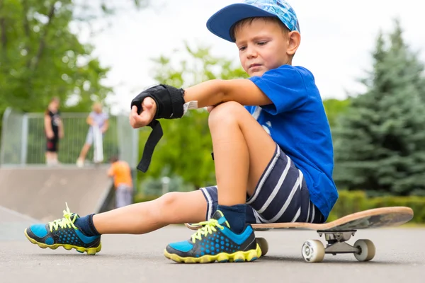 Boy on Skateboard Adjusting Elbow Pad in Park