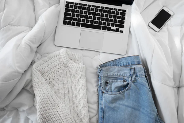 Female outfit, a  smartphone and a laptop laid out on bed, morni