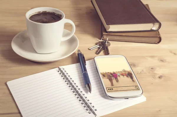 Still life photo of smart phone with travel search, notebook, coffee, book, pencil and keys on wooden table.
