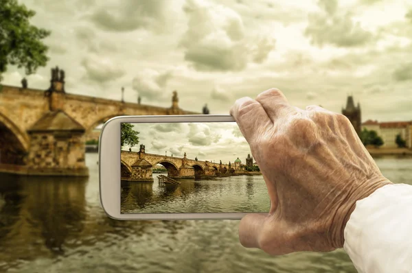 Old hand takes a picture of Charles Bridge in Prague, Czech Repu