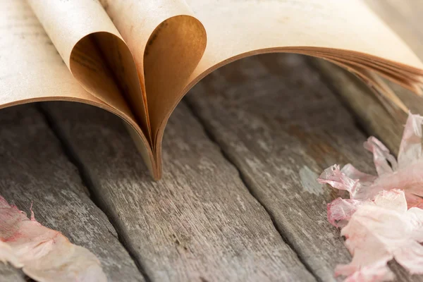Heart shape from opened book pages on wooden background.