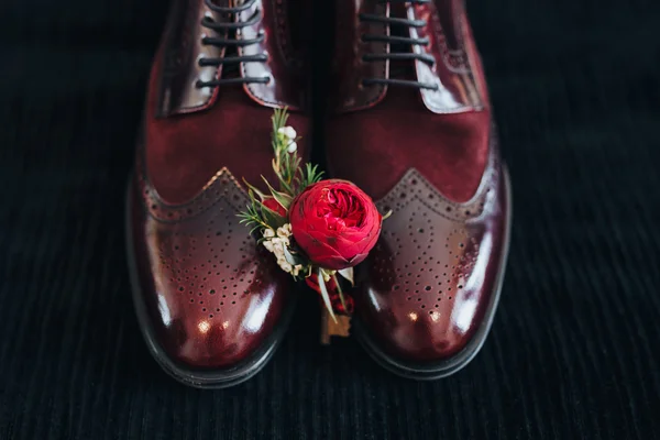 Wedding. groom shoes. Boutonniere. Artwork. Grain. Groom boutonniere of red flowers and greenery lies on the groom\'s leather shoes