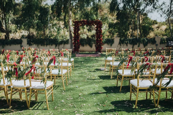 Wedding. Ceremony. Grain. Artwork. Chairs gold color stand on the lawn in the area of the wedding ceremony. On chairs decoration of greenery and tissue tapes