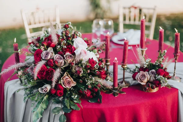 Wedding. Banquet. Grain. Artwork. At the banquet table with tablecloth colors Marsala, is the composition of flowers and greenery, cutlery and candles