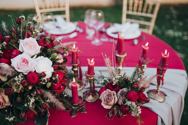Wedding. Banquet. Grain. Artwork. At the banquet table with tablecloth colors Marsala, is the composition of flowers and greenery, cutlery and candles