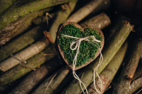 Wedding rings on a wooden board in the form of heart on a bed of moss on the background of logs