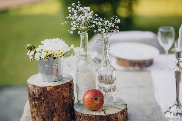 Wild flowers in glass bottles and metal buckets on the festive table, wedding table