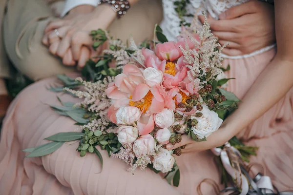 Couple sitting on the grass and holding a bouquet of pink and white peonies and green