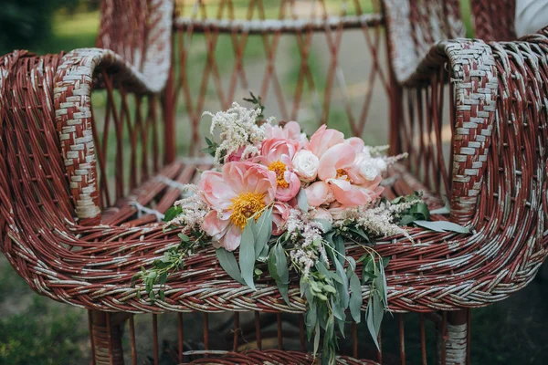 Bouquet of pink and white peonies and green is in a vintage garden chairs on the background of green garden