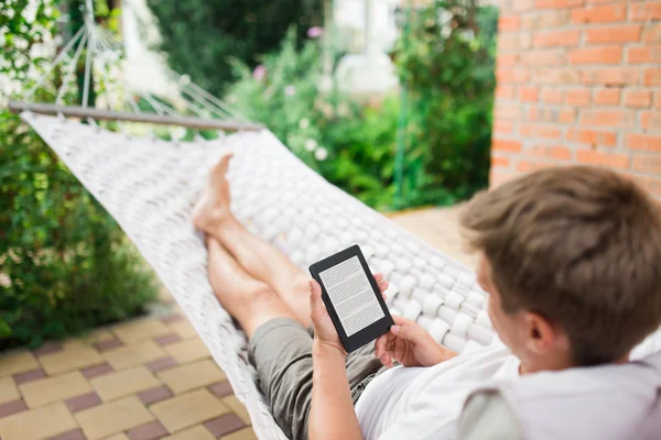 Man using e-book with lorem ipsum text on screen while relaxing in a hammock.