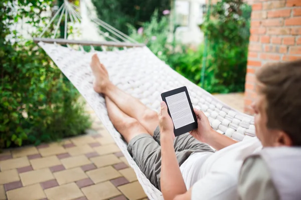 Man using e-book with lorem ipsum text on screen while relaxing in a hammock.