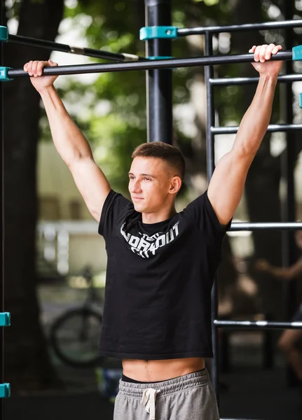 Young man doing pull ups on horizontal bar outdoors, workout, sport concept