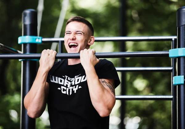 Young man doing pull ups on horizontal bar outdoors, workout, sport concept