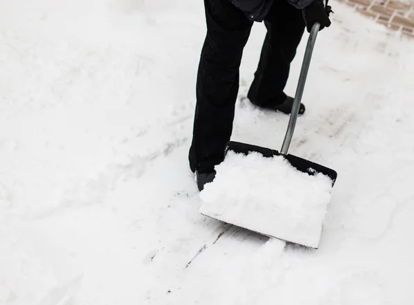 Man with snow shovel cleans sidewalks in winter