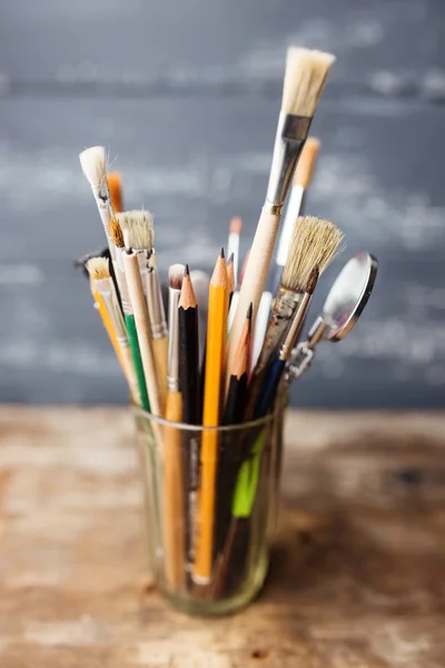 Photo of paint brushes in a glass standing on old wooden table,