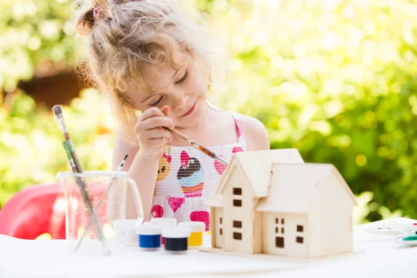 Portrait of little girl paints wooden model of house,  summer ou