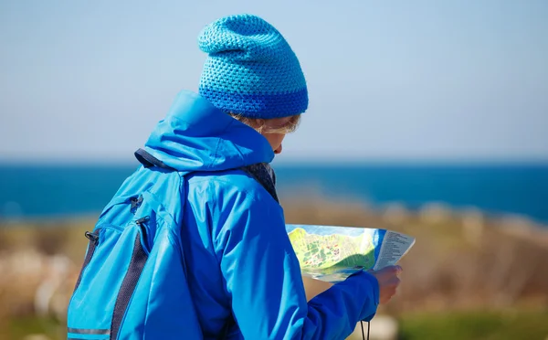 Young woman checking map in seashore on hiking trip. Travel conc