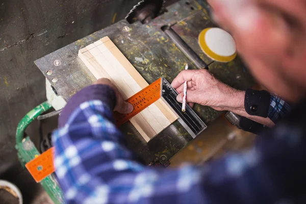 Old carpenter taking measurement of a wooden plank