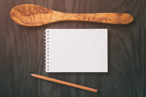 Notepad with pencil and wood utensils on wood table