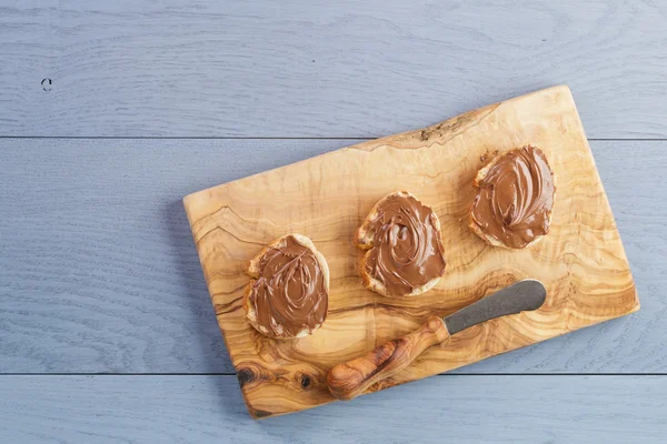 Baguette slices with chocolate hazelnut spread on olive board from above