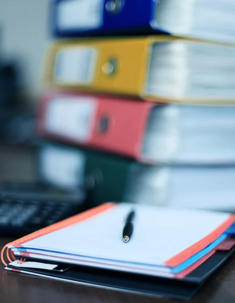 Note book and pen on desk with files on background