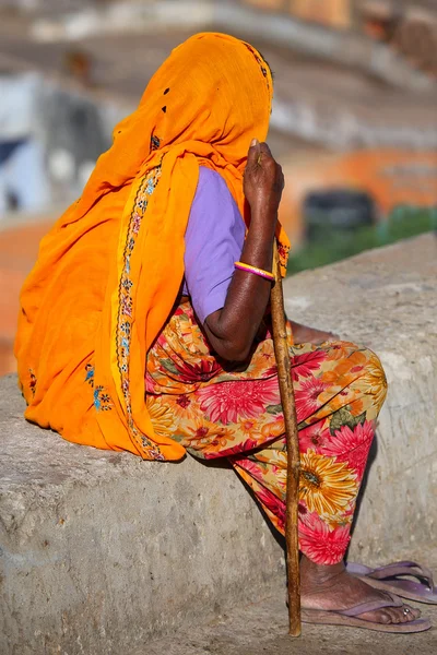 Local woman in colorful sari sitting on a stone wall, Jaipur, In