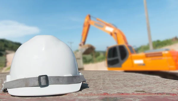 Safety engineering and a helmet resting on the details of the construction site with a bulldozer behind them.