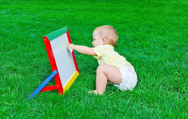 Beautiful little baby  draws sitting on a lawn