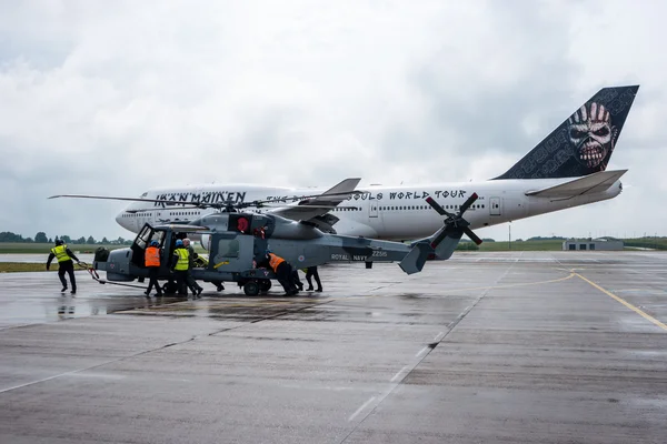 A helicopter AgustaWestland AW159 Wildcat. Black Cats (Royal Navy Display Team) in the foreground and Iron Maiden\'s Boeing 747 \