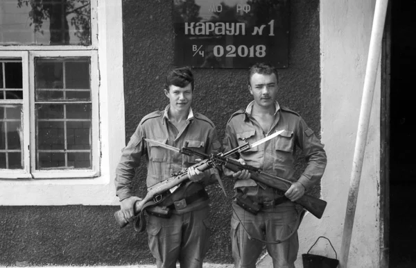 A soldiers posing with guns. The inscription in Russian: Russian Defence Ministry. Guard 1, the number of military unit 02018. Film scan. Large grain