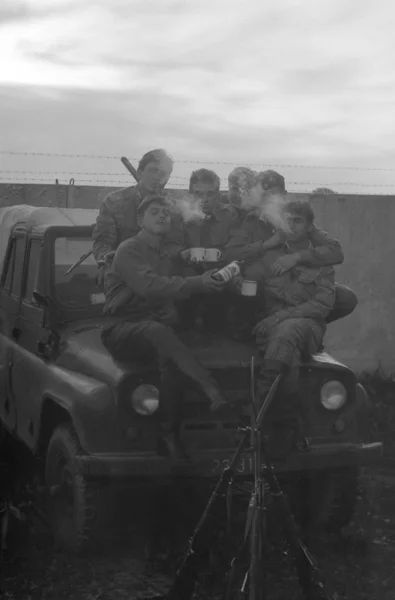 A group of soldiers with weapons near the army SUV UAZ-469. Film scan. Large grain