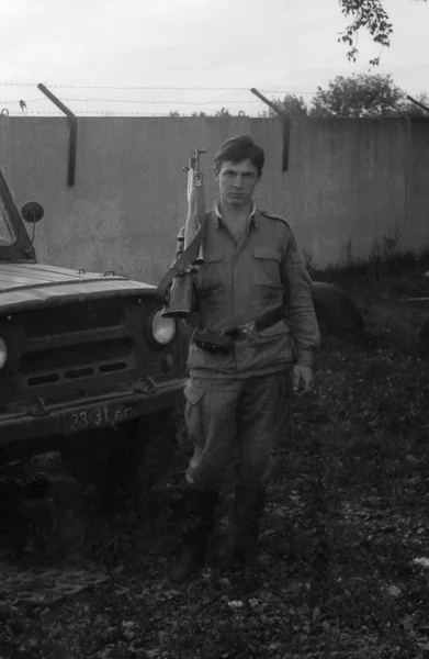 A soldier with a gun standing near army SUV UAZ-469. Film scan. Large grain