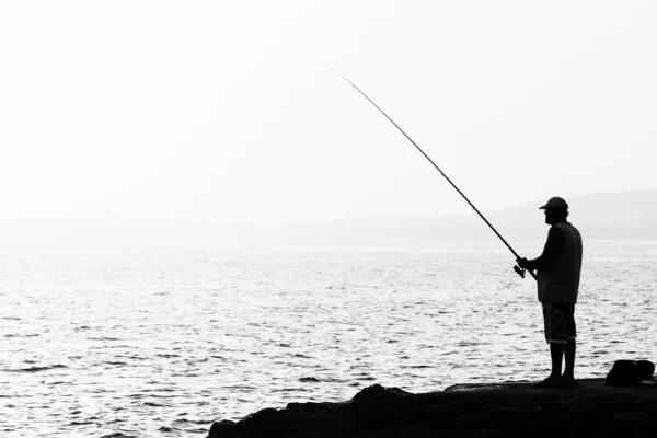 Evening fishing. Lone fisherman fishing from the shore. Black and white.